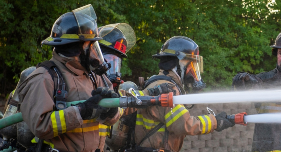 fire fighter in uniform holding fire hose standing next to a fire truck