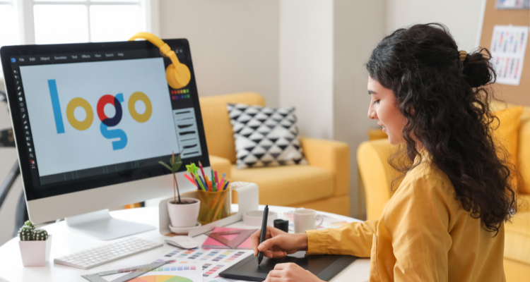 Graphic designer working at a desk creating a logo on a computer using a digital drawing tablet