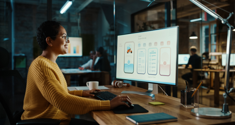 Student working at a desktop computer designing a mobile app interface in an interactive design workspace