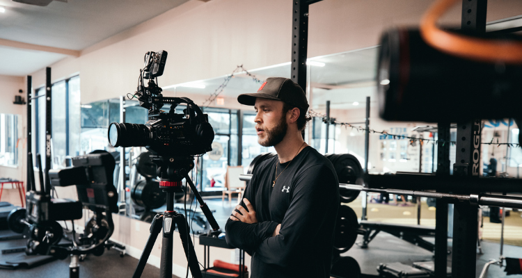 Student filming video content with a professional camera on a tripod inside a studio or gym setting
