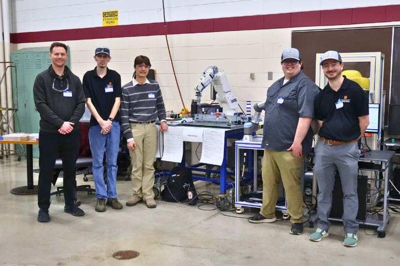 Students from the IOPP club gather around their group assignment, a pick and pack robot and PLC unit.